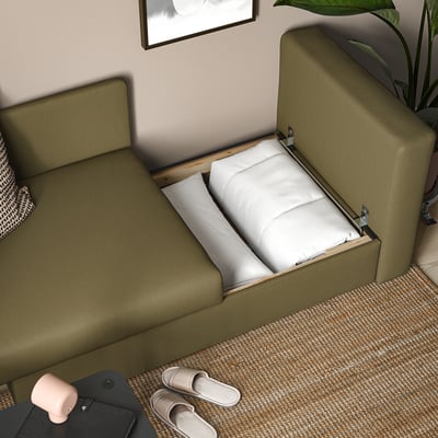 Olive sofa bed with open storage compartment, pillows inside, on textured rug.