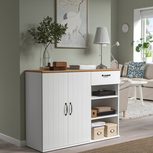 SKRUVBY white wooden sideboard with open shelves, drawer, and doors. Stands against green wall with decor, fits well in living room.