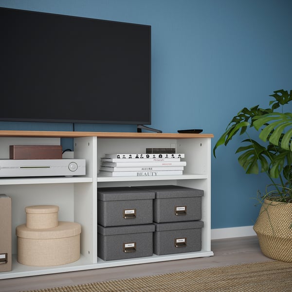Modern tv stand with open and closed storage, housing electronics, books, and decor against blue wall.