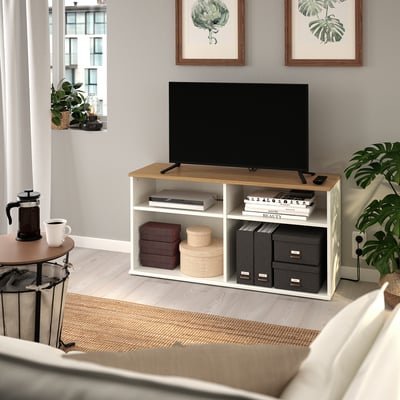 Wooden tv bench with white frame, tv, books, and coffee maker in a cosy living room.