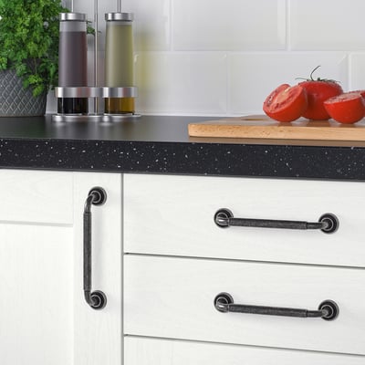 Kitchen cabinets with anthracite handles. Two large red tomatoes on a wooden board, three spice dispensers, and a green plant beside.