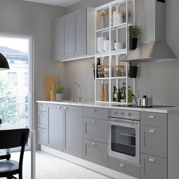 Modern kitchen with grey SKYDRAG led lights. Cabinets, oven, and open shelves. Small plants, dishes, and bottles decorate. Window to the left.
