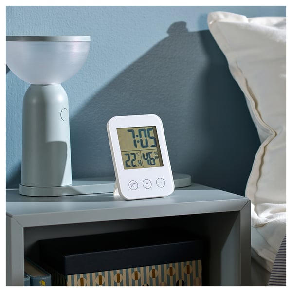 Bedside, white clock and lamp. Clock shows time, date, and humidity. Lamp modern, ribbed design.