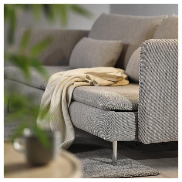 A grey SÖDERHAMN sofa bed with light cushions, a cosy blanket, and a book on it, set on a modern rug.