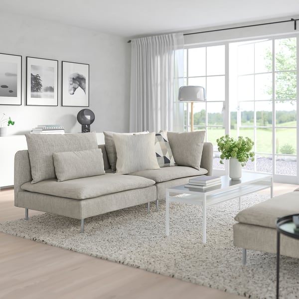 Modern minimalist living room with large grey SÖDERHAMN sofa, low coffee table, and large windows showing green outdoors.