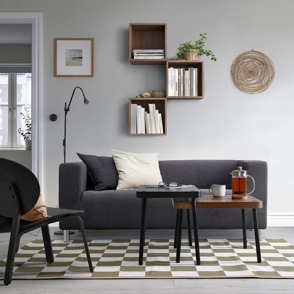 Modern living room with grey sofa, coffee tables, bookshelves, and rug. Black SONHULT nest tables beside sofa.