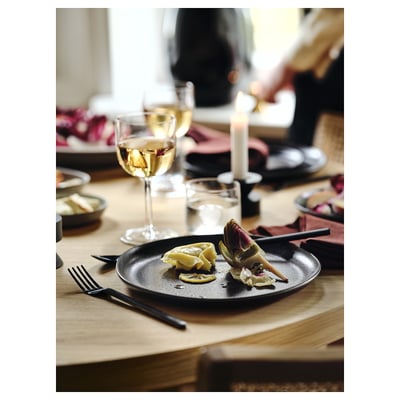 Dinner table with black cutlery, plate of artichoke, and wine glasses.