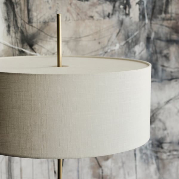 Cylindrical lamp with cream-colored shade and brass stem on travertine base, exuding elegance and stability.