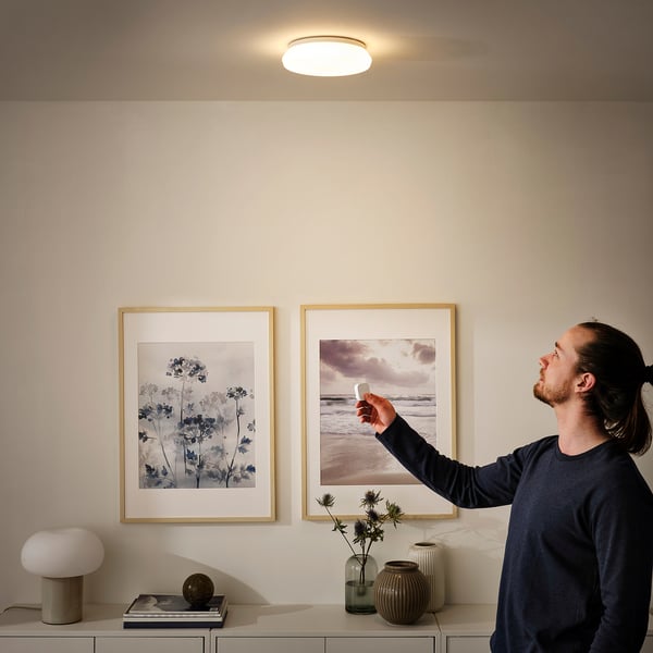 Person adjusting wireless dimmer near wall art, featuring small lamp with integrated lighting.