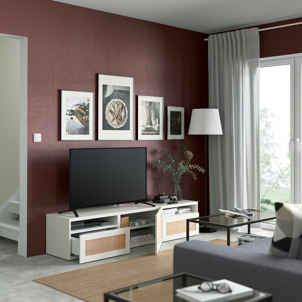 Modern living room with burgundy walls, white tv stand, flat screen tv, lamp, and glass coffee table with magazines.