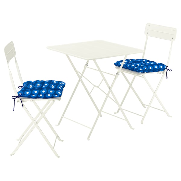 White metal outdoor table with two folded chairs, blue cushions.