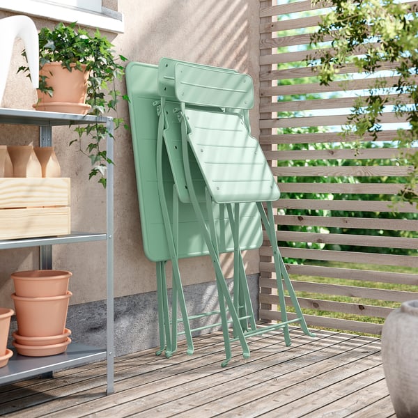 Three light green SUNDSÖ foldable chairs rest against a wall near a wooden fence. Perfect for small spaces.