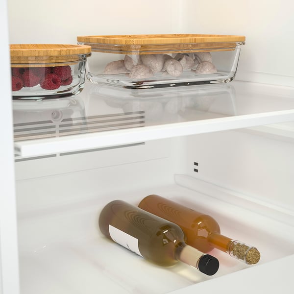 Fridge interior with clear containers: one has berries, another has baking items. Bottles stored below.
