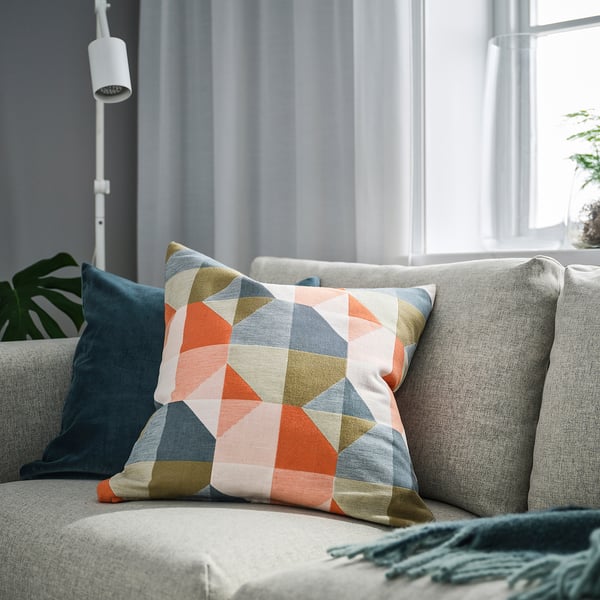 SVARTHÖ cushion cover in geometric pattern, textured, colourful, sitting on grey sofa near window.