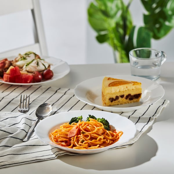 Three meals on a table: chicken & veggies, spaghetti, cheesecake. Water and cutlery.