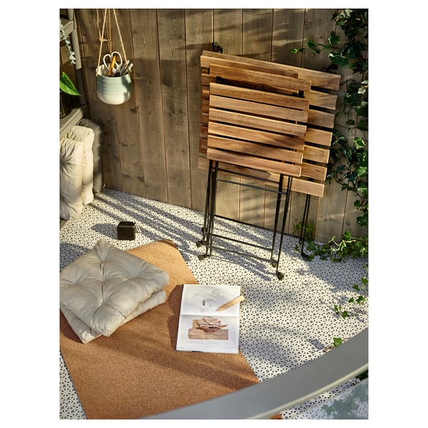 Cosy balcony setup with TÄRNÖ wooden table & chair in natural wood, cushions, and books on a patterned rug.