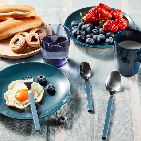 Blue-handled cutlery set on a breakfast table with plates of food and mugs.