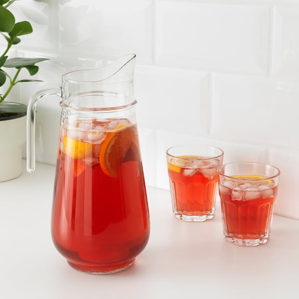 Clear glass pitcher with handle, filled with red liquid and ice, next to two filled glasses.