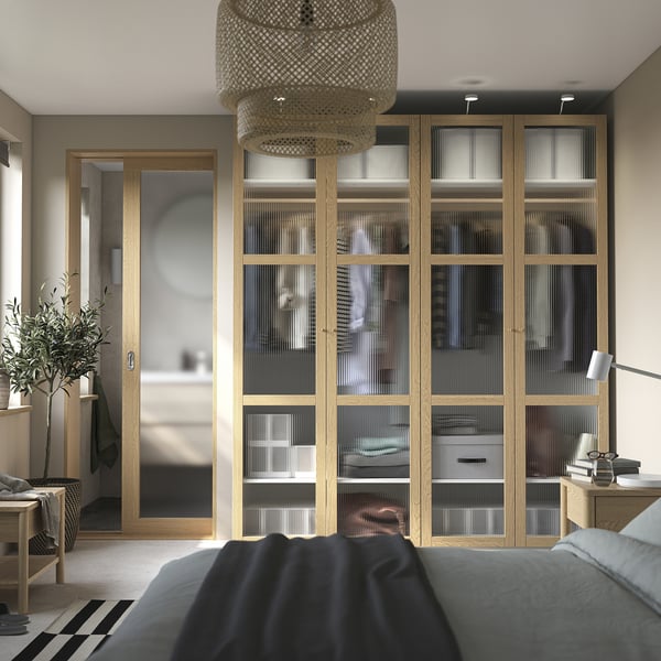 Modern bedroom with glass doors in light oak wardrobe, grey bed, and pendant lamp.
