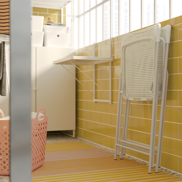 Bright, small room with yellow-tiled walls and striped rug. Includes white plastic folding chair and pink laundry basket.