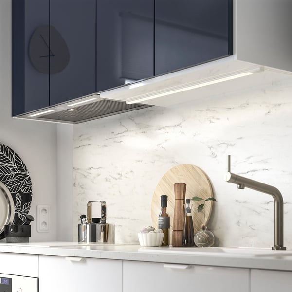 Modern kitchen with marble backsplash, stainless sink, black utensils, wooden board, and range hood.