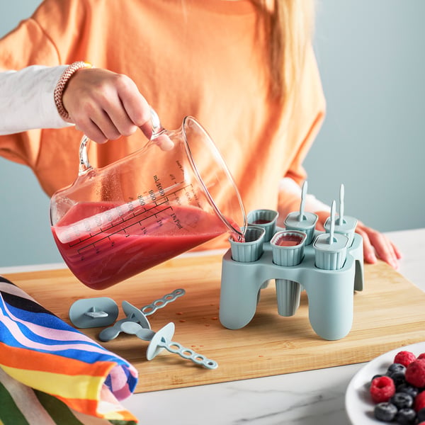 Person pours juice into ice pop moulds on a wooden board.