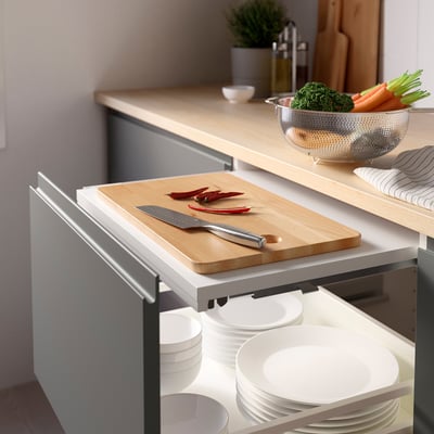 Modern kitchen setup with pull-out cutting board, knife, and vegetables on counter.