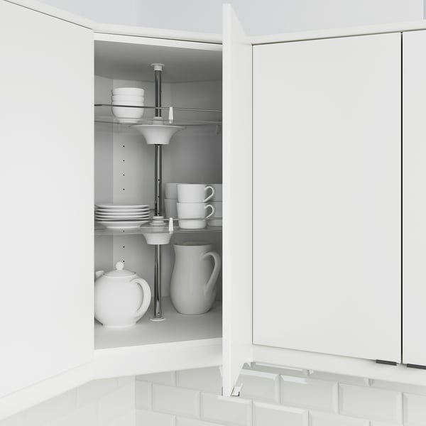 White corner cabinet with swivel shelves holding plates, cups, and teapot.