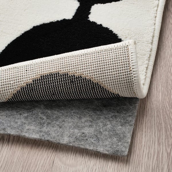 Black and white rug corner on wood floor, showing underlay for grip.