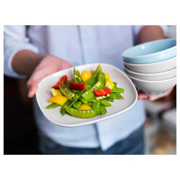 A person holding a square white VÄRDERA plate, filled with colourful vegetables. Soft, rounded edges; durable feldspar porcelain.