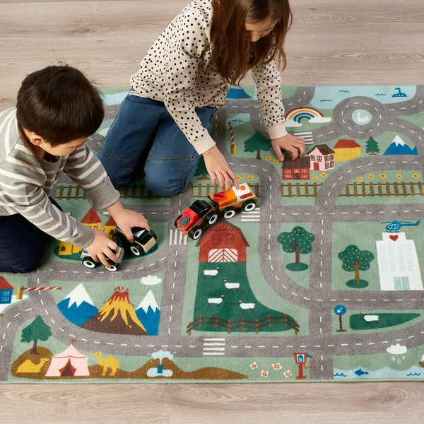 Kids play with toy cars on a colourful, textured rug simulating town, desert, and mountains.