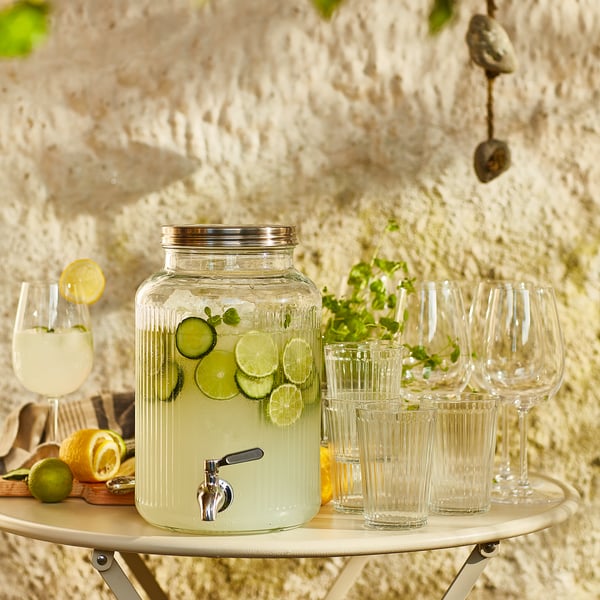 Clear glass VARDAGEN beverage dispenser with stainless steel tap, lime slices, mint, on wooden tray with clear glasses.