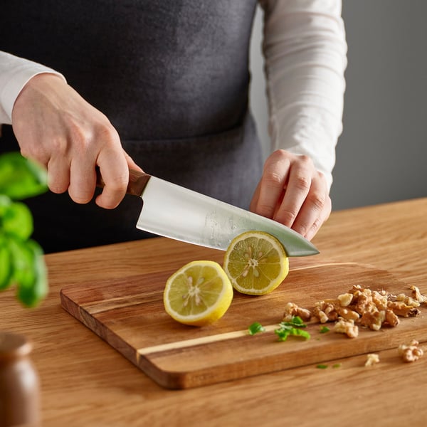 Person slices lemon on wooden cutting board with VARDAGEN knife. Lemons and walnuts present.