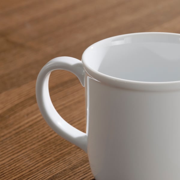 Clean white mug on wooden table, smooth handle, bright finish.