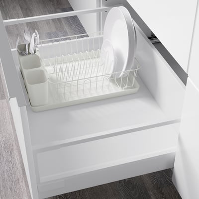 White dish drainer with removable tray inside cabinet to collect water.