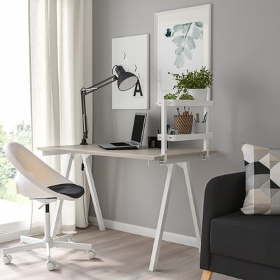 White VATTENKAR desk by window with tech devices, lamp, and plants. Chair tucked under, black sofa with pillow.