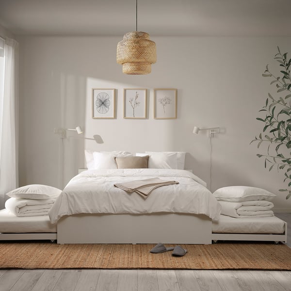 Modern bedroom with white VIHALS bed, two trundles, clean lines, pendant light, botanical prints, and wall lamps. Jute rug and large plant.