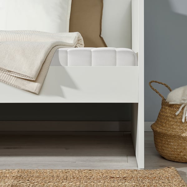 Modern white daybed with folded mattress, basket of blankets beside, minimalist design.