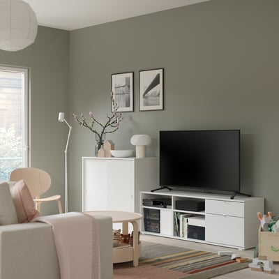 Modern living room with green walls, white furniture, and flat-screen tv, with wooden toys and colourful rug on the floor.