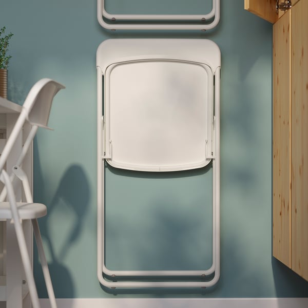 Foldable dining chair mounted on wall, shown in white, ready for space-saving storage.