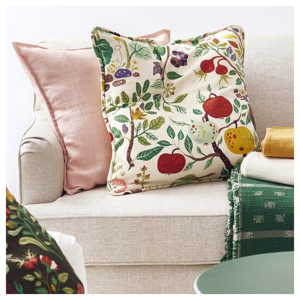 A cosy sofa with a floral-patterned pillow in red, green, and yellow tones, and a light pink pillow on a green blanket.