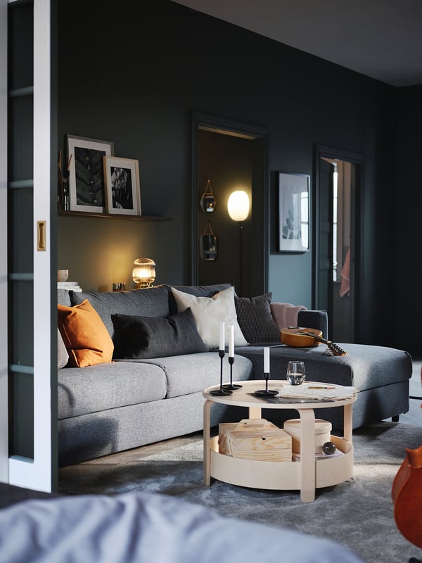 Modern living room with VIMLE grey sofa, orange cushions, wooden coffee table,arlamp, dark walls, white doors, black and white framed art.