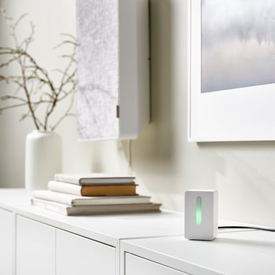 Small VINDRIKTNING white air quality sensor on cabinet, green light on, next to books and vase.