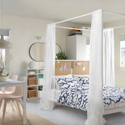 Modern bedroom with VITARNA bed, patterned bedding, and curtains. Includes pegboard wall, mirror, and dining table with pink chairs.