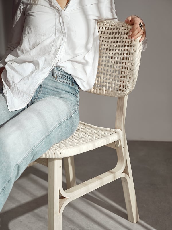 Person sitting on a light-colored wicker chair wearing a white shirt.