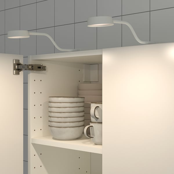 Modern cabinet lamp with flexible neck directs light onto shelves, illuminating stacked bowls and mugs. Slim design suitable for tight spaces.
