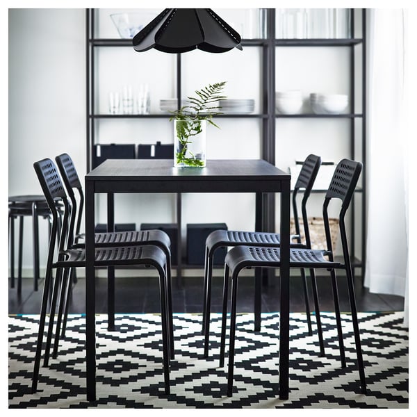 Modern black dining set with square table, four stackable chairs, and geometric rug; minimalist design.