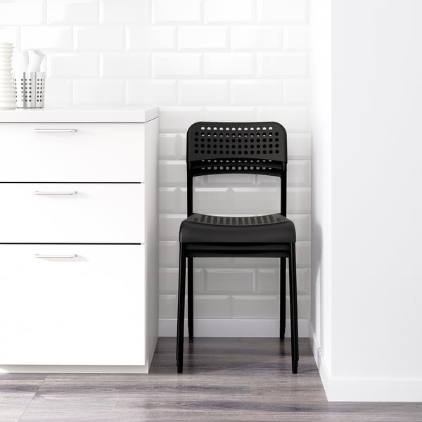 Black plastic chair with perforated design, suitable for stacking and indoor use, positioned near white cabinets.