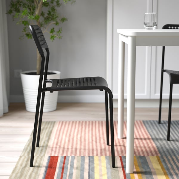 Black stackable chair ADDE next to white table on striped rug, suitable for indoor use.