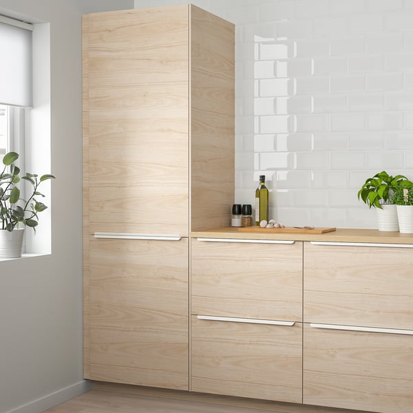 Modern light wood kitchen with sleek cabinets & white backsplash. Plants on countertop.